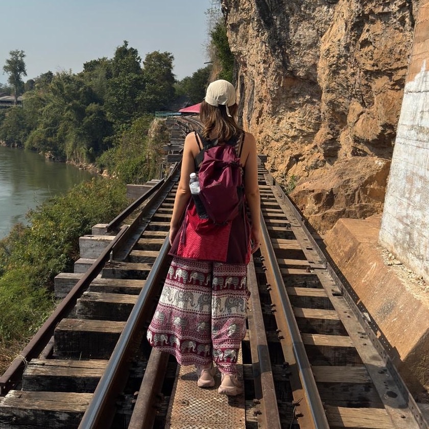 Alice walking along a railway track above a river in Thailand